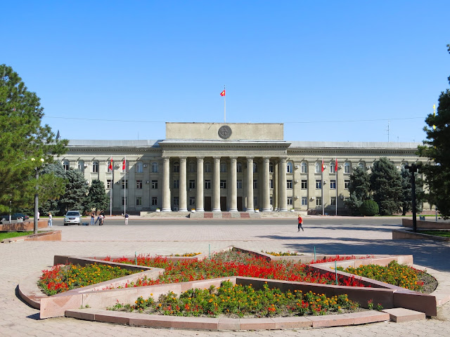 Prédio do antigo Parlamento em Bishkek, no Quirguistão, com canteiro de flores vermelhas à frente