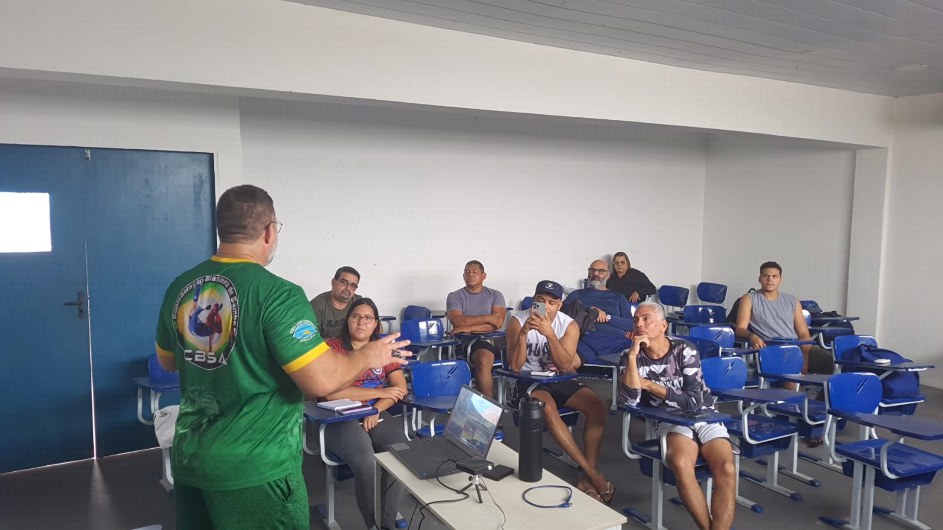 Instrutor da CBSA, de camisa verde, dá aula teórica em sala para os participantes do curso