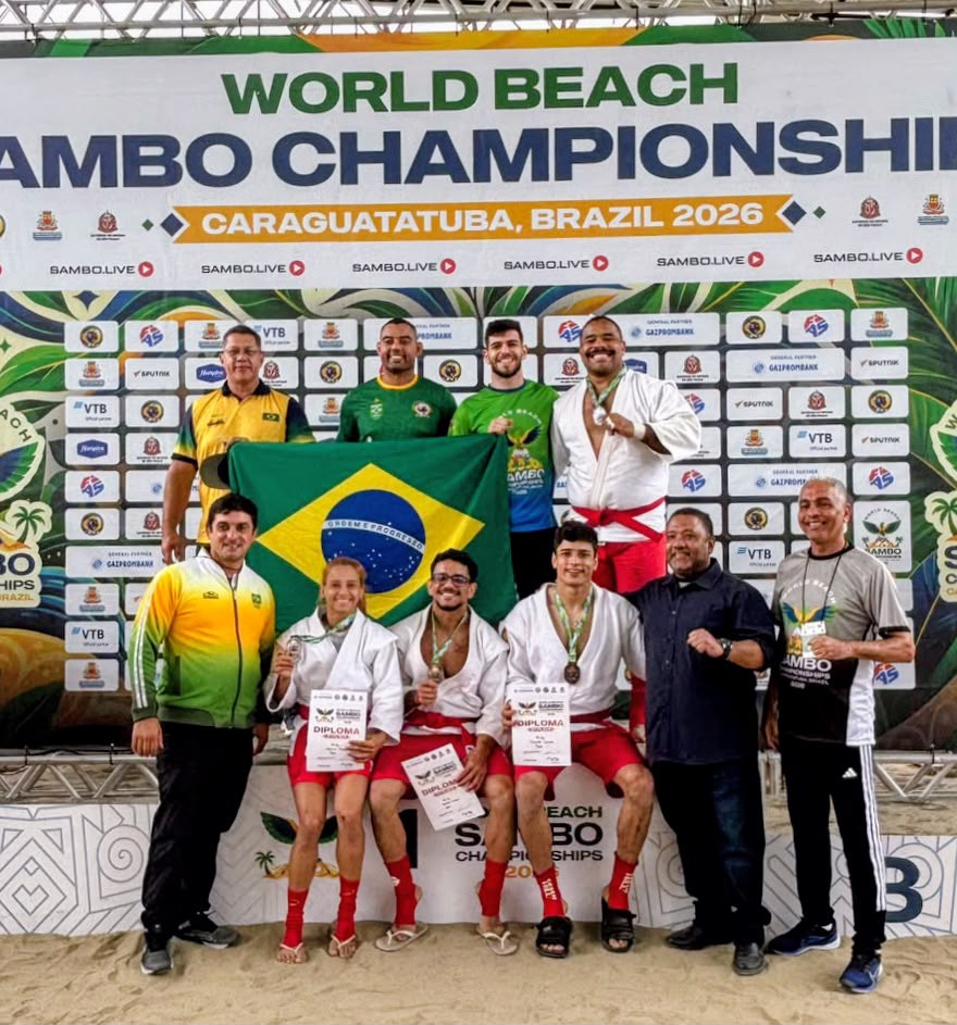 Delegação brasileira no pódio do Mundial de Sambo de Praia 2026, exibindo diplomas e medalhas ao lado da bandeira do Brasil
