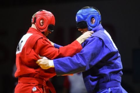 Dois atletas de SAMBO para cegos, de vermelho e de azul, com capacetes e vendas nos olhos, em pegada
