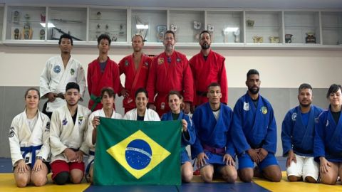 Turma do curso técnico, de quimonos brancos, vermelhos e azuis, com a bandeira do Brasil no tatame