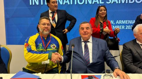 Adalberto Corrêa, de agasalho da seleção brasileira, aperta a mão do presidente da FIAS, Vasily Shestakov, no congresso em Yerevan, Armênia