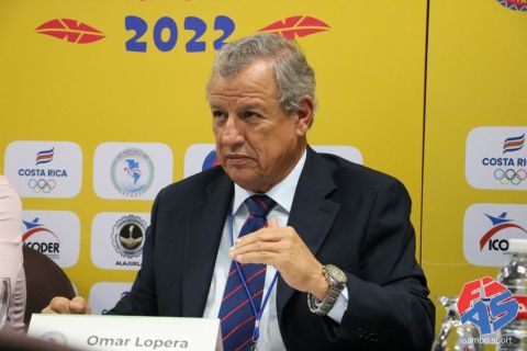 Omar Lopera, então presidente da União Pan-Americana de Sambo, de terno, sentado à mesa diante de painel com logos de entidades esportivas